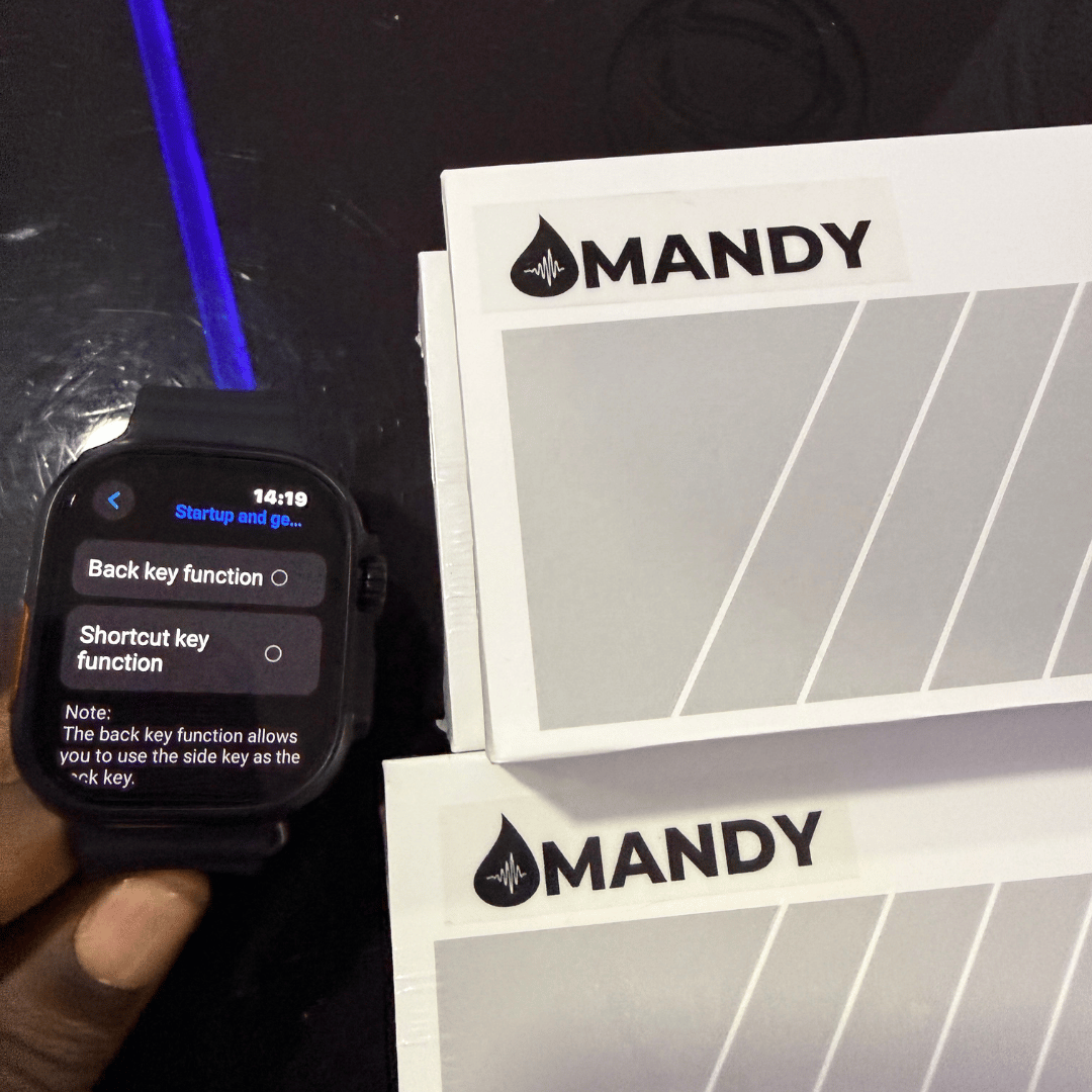 Mandy Android Smartwatch M12 with a screen displaying settings next to MANDY branded materials on a dark surface.