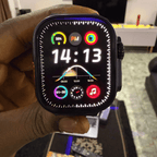 Mandy Android Smartwatch M12 with a colorful display held in a hand, blurred indoor background